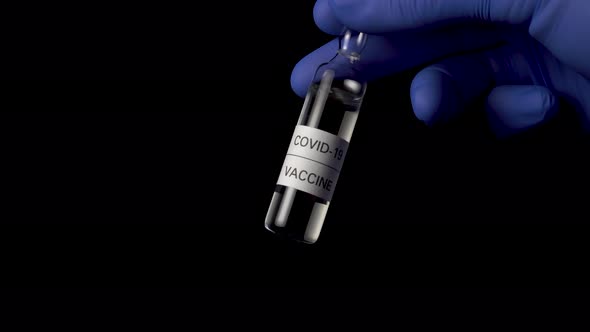 Ampoule of coronavirus vaccine on a black background in the hands of a doctor