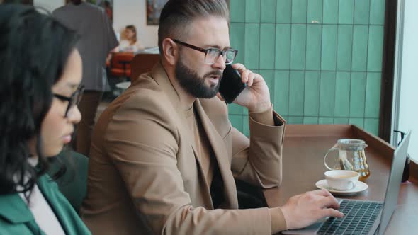 Businessman Talking on Phone and Using Laptop in Cafe