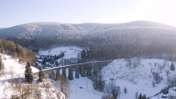 Winter countryside with a stone train viaduct in falling snow,sunny.