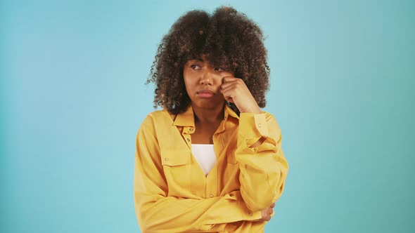 Young Darkskinned Woman Acting Like Crying Propping Her Face By Hands While Posing Against Blue