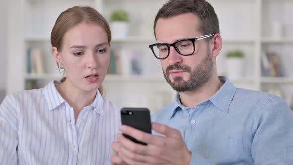Portrait of Serious Young Couple Using Smartphone Together 