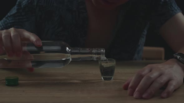 Drunk, Depressed Asian Man Pouring Vodka In A Shot Glass Before Drinking In Black Background