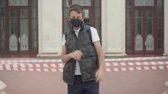 Happy Boy in Covid-19 Face Mask Dancing in Front of Closed School and Showing Victory Gesture