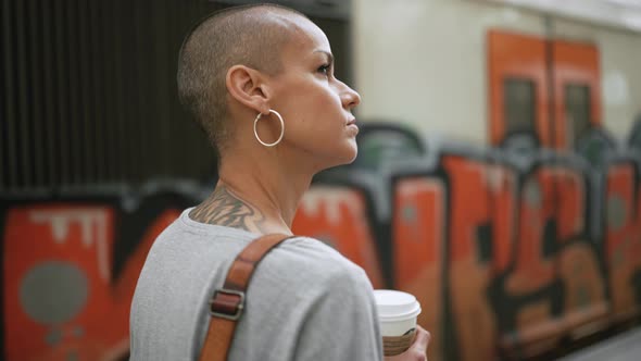Confident bald woman wearing t-shirt walking with cup of coffee