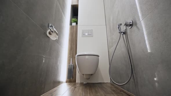 Camera Zooming Out From Ceramic Flush Toilet Inside Narrow Restroom with Tiled Walls in Modern