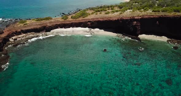 Drone shots of a cliff side beach with blue waters and no one around.