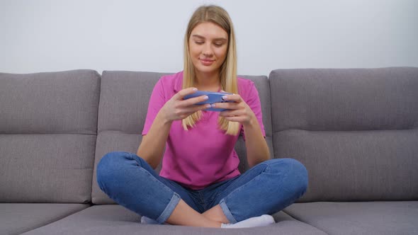 Young adult blonde girl playing video game on mobile phone with smile in 4k video