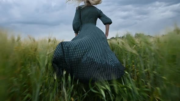 Young Happy Blonde Girl Runs on a Green Wheat Field in the Evening Against the Background 