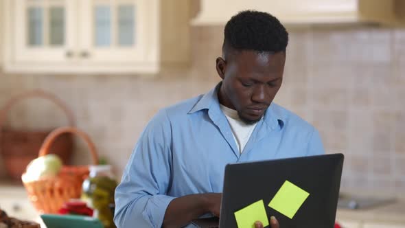 Thoughtful Concentrated African American Man Surfing Internet on Laptop Searching Recipe Online