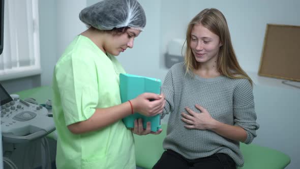 Happy Pregnant Young Woman Watching Ultrasound on Tablet Talking with Doctor in Hospital