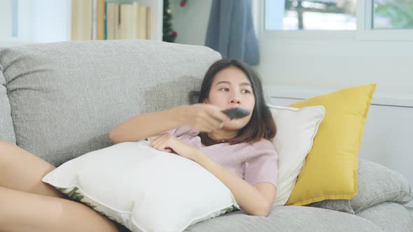 Young Asian teenager woman watching TV at home, female feeling happy lying on sofa in living room
