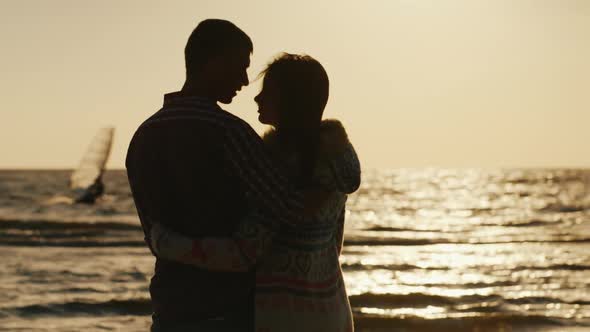 Silhouette of a Loving Couple, Hugging at Sunset Near the Sea. Sailboat Floats in the Distance