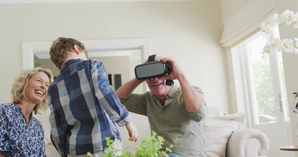 Happy senior caucasian couple with grandson using vr headset in living room