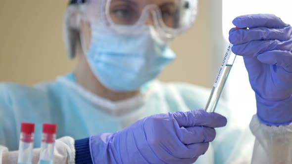 Professional Female Scientist Wearing Glasses and a Mask Holds a 2019Ncov Coronavirus Vaccine Sample