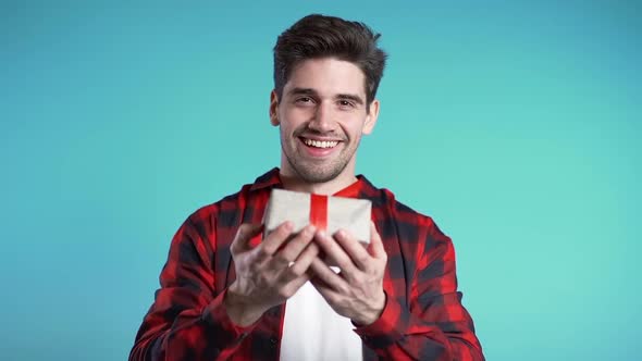 Handsome Man Holding Christmas Gift and Gives It by Hands It to Camera. He Is Happy, Smiling