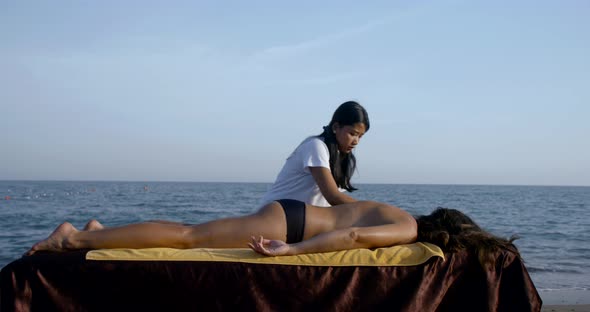 Tourist Woman Is Relaxing During Session of Traditional Thai Massage on Sea Shore in Summer Day