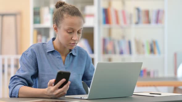 African Woman Using Smartphone and Laptop in Library