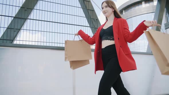 Sexy smiling woman in red jacket walks with shoping bags in the city urban street. Steadicam stabili