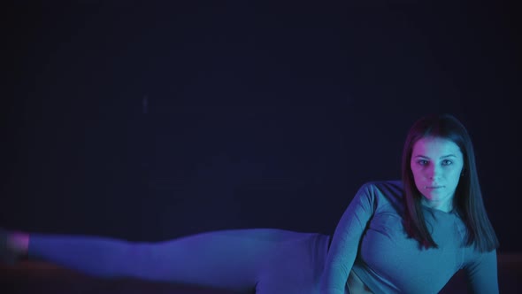 Young Woman in Sports Costume Stretching Her Leg and Doing an Exercise in Neon Lighting