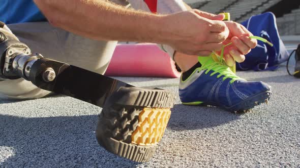 Low section of caucasian disabled male athlete sitting, tying shoe