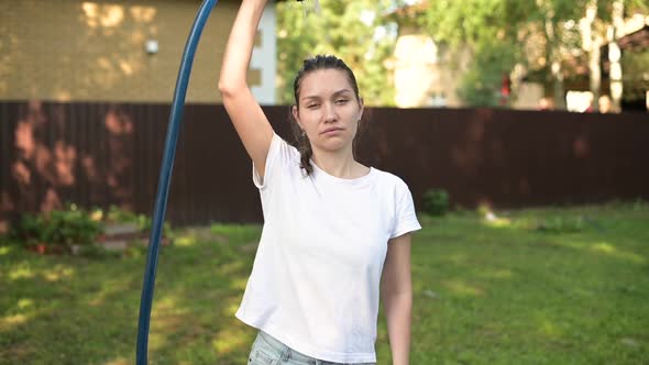 Young woman cools herself on a hot sunny day by pouring water from a garden hose