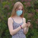 A young girl in a protective medical mask looks at the phone and sends messages - VideoHive Item for Sale