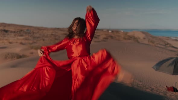 An Asian Woman in a Red Dress Dancing on Sand Dunes