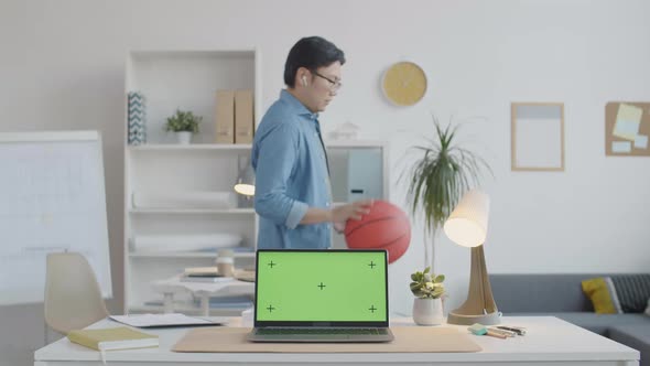 Asian Man Dribbling Basketball in Office