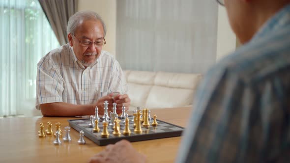 Asian Senior Elderly male playing chess game with friend together enjoy retirement life at home.