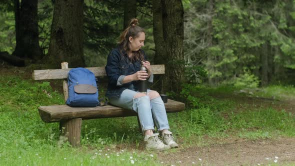 Woman backpacker traveler drinking hot tea and relaxing on the bench in park forest