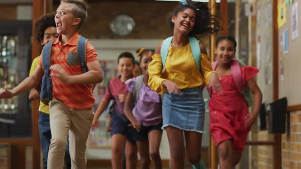 Diverse group of happy schoolchildren wearing backpacks, running fast through school corridor