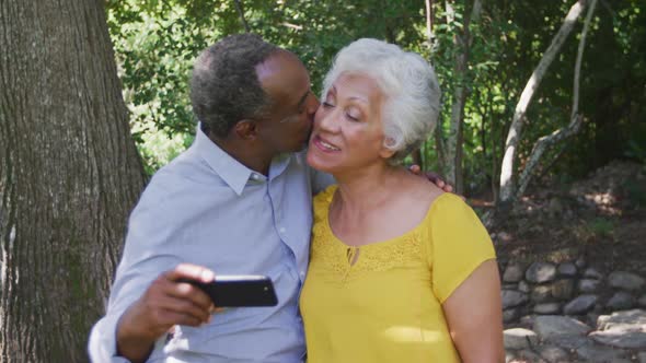 Senior African American husband and mixed race wife laughing and taking photo in the garden