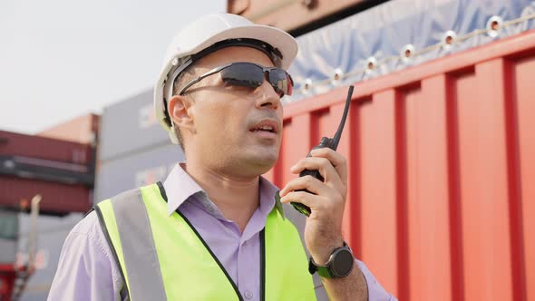 Engineer foreman talking on walkie-talkie with colleague in container warehouse