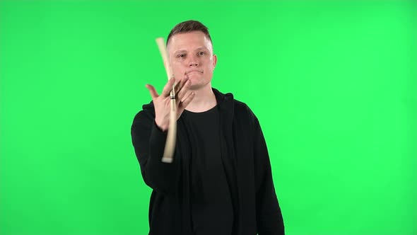 Portrait of a Drummer Spinning Drumsticks Professionally. Young Guy in a Black Jacket on a Green