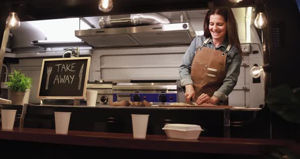 Caucasian chef woman working inside food truck at night time preparing dinner food