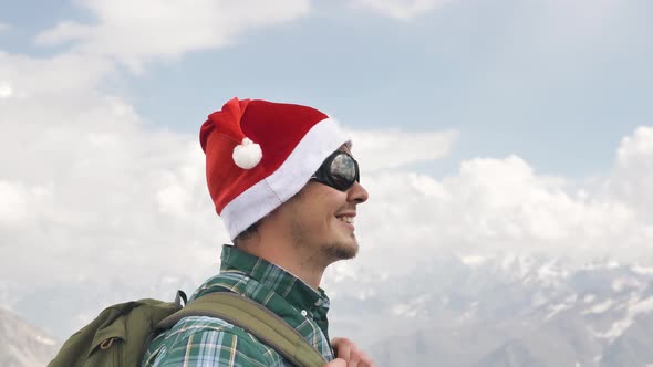 A Young Happy Male Tourist in a Christmas Hat and Glasses Stands Looking Around Smiles and Goes on