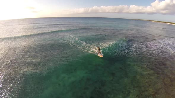 Aerial shot of young woman sup standup paddleboard surfing on a wave in the Caribbean.