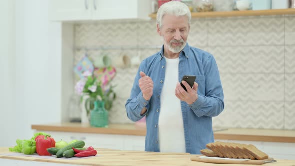 Old Man Doing Video Call on Smartphone While Standing in Kitchen