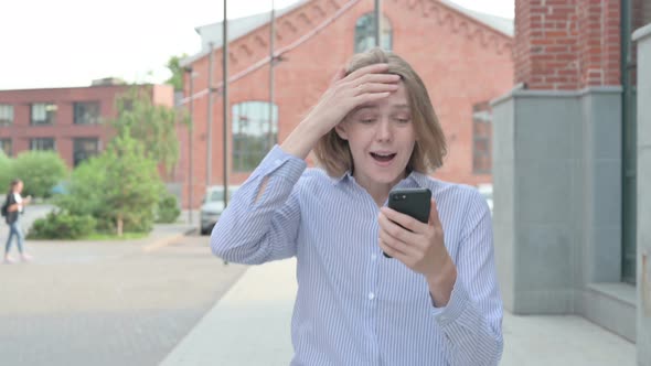 Woman Reacting to Loss on Smartphone While Walking in Street