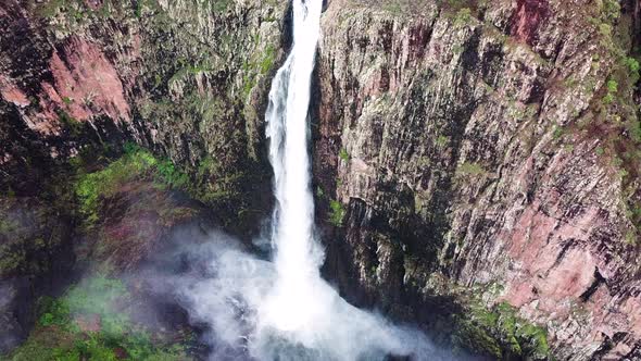 Drone flying towards huge waterfall, camera tilts down for amazing perspective.