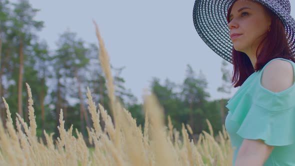 Young Woman in Dress and Hat Standing in Wheat Field