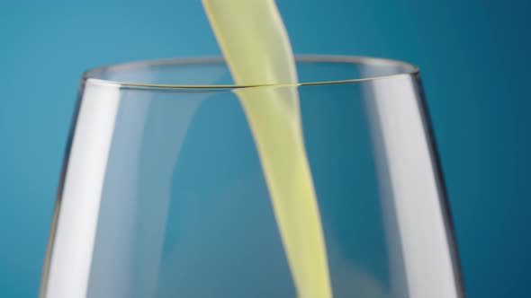 Macro Shot of a Glass with Pouring Freshly Squeezed Natural Orange Juice on a Blue Background