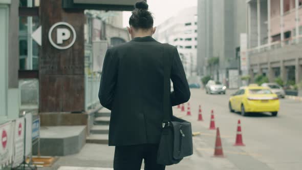 Asian businessman casual dress carrying a shoulder bag while walking in the street.