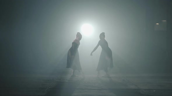 Two Graceful Professional Ballerinas Dancing Elements of Classical Ballet in the Dark