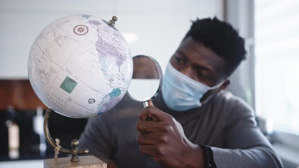 Young Black Man with Face Mask Looking at the Through Magnifying Glass. Travel Ban During Global