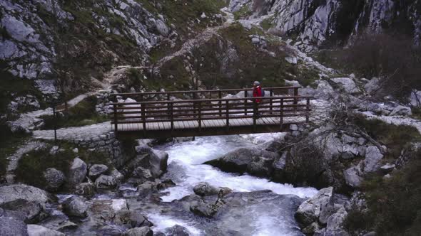 Active tourist with backpack walking on bridge above mountain river