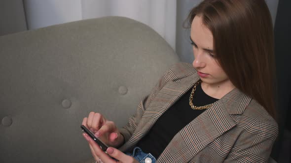 Portrait of Woman Using Phone Watching Content Browsing Internet Has a Headache Sitting on Couch at