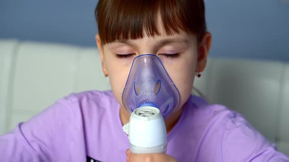 Little Girl Makes Inhalation with Medical Nebulizer While Sitting at Table and Looking to Camera
