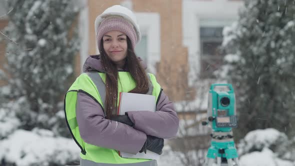 Middle Shot of Confident Positive Female Surveyor Geodesist Standing Outdoors Looking at Camera and