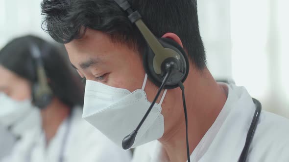 Close Up Of An Asian Man Doctor In Masks Working As Call Centre Agent And Speaking To Customer